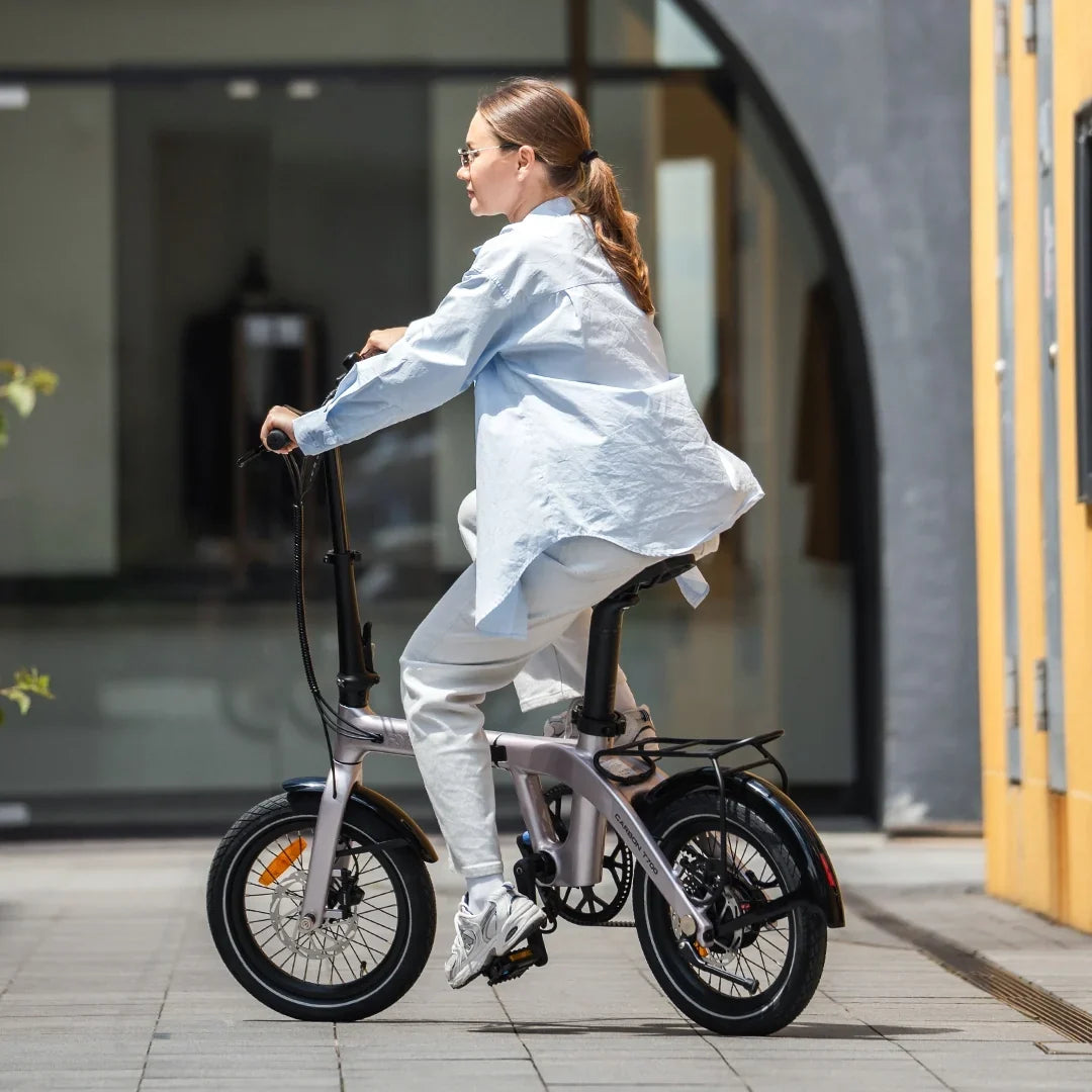 Woman riding RYD Aero 16 carbon folding electric bike through a city street corner with smooth handling and urban mobility