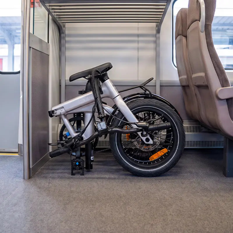 Folded RYD Aero 16 electric bike stored on a luggage rack for convenient train travel