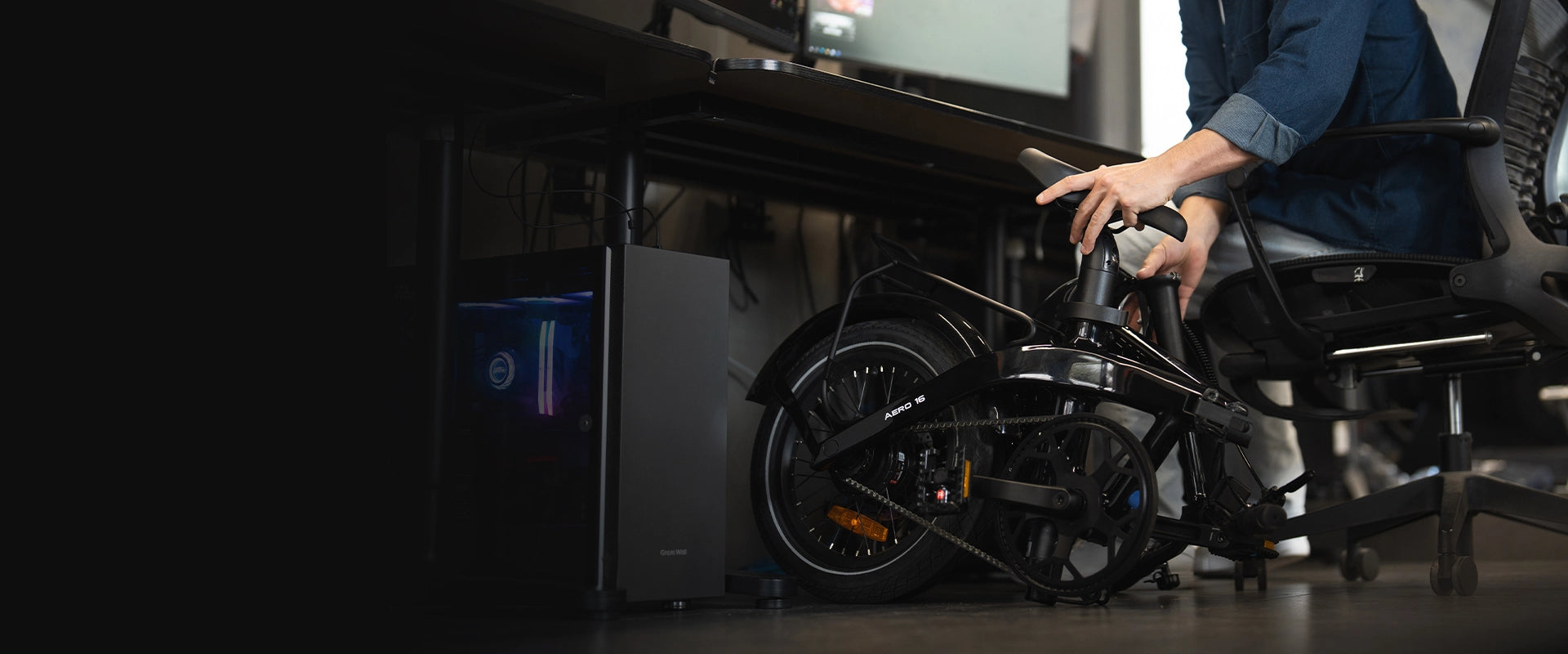Commuter storing a folded black RYD Aero 16 carbon folding electric bike under an office desk beside a computer